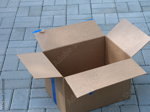 An empty cardboard box lying on tiles outside. Close up.