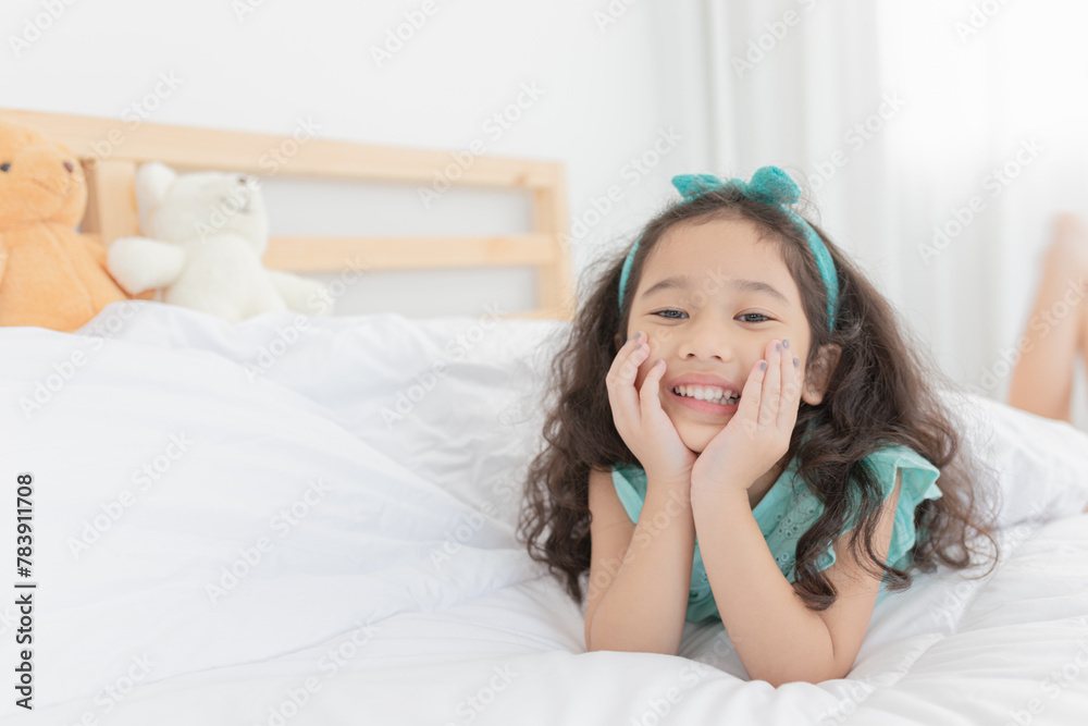 attractive asian children relax on white bedroom, she smiling and feeling happy, she rest chin on her hand, curly hair attractive asian children relax on white bedroom, she smiling and feeling happy, she rest chin on her hand, curly hair