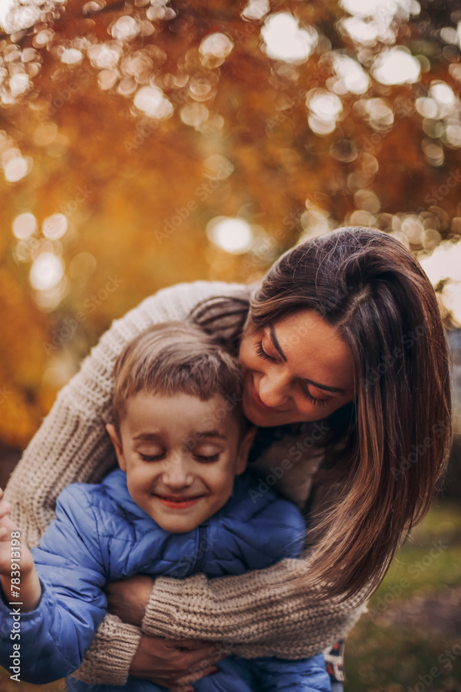 Obraz premium Young happy family, mother and little son child walking in autumn forest, kid holding yellow tree leaf in hand