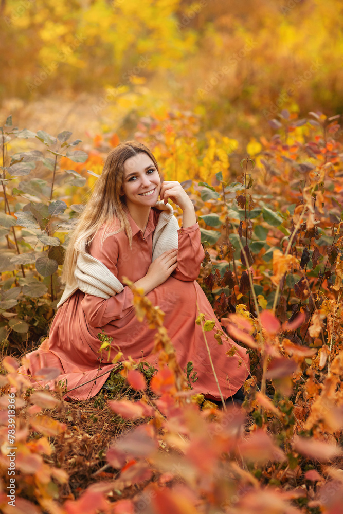 Beautiful young blonde woman in dress sitting with pensive look in tall grass in autumn forest Beautiful young blonde woman in dress sitting with pensive look in tall grass in autumn forest