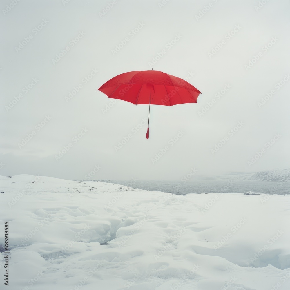Surreal outdoor scene with a red umbrella levitating over a snowy landscape under a cloudy sky