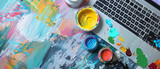 Commercial A vibrantly colored paint palette with fresh paint dabs rests beside a digital drawing tablet with a stylus pen and a modern laptop displaying a website design mockup