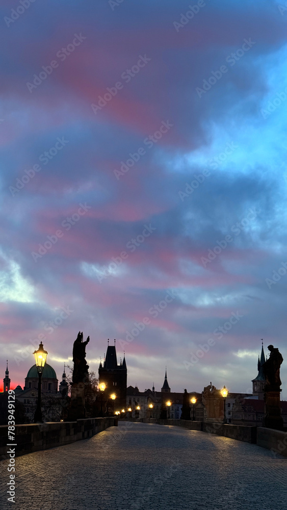 Prague's Charles Bridge at dawn: Street lights gleaming under pink-grey skies.