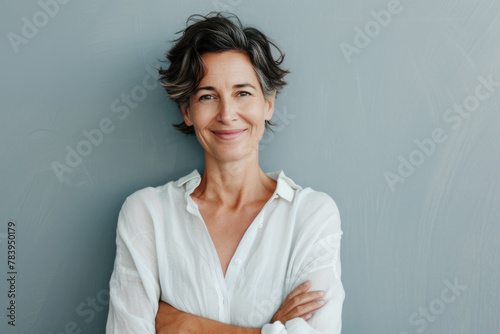 Portrait of a smiling confident woman in her forties, with crossed arms in front of a grey wall background photo