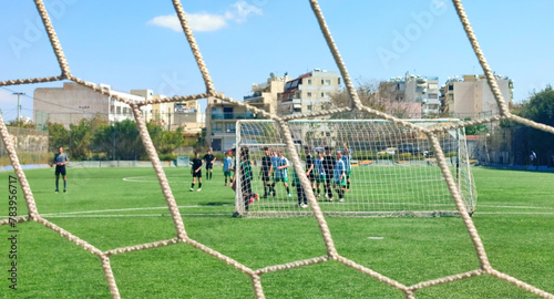 Photo of a kids Sunday football league match behind a goal net. Conceptual image. 