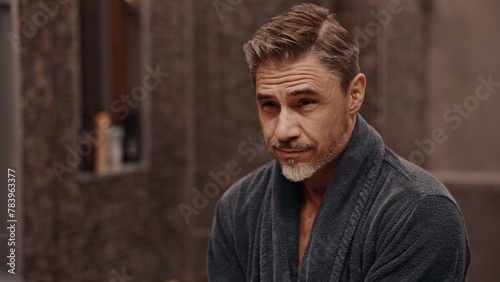 Confident mature male standing in front of a bathroom mirror. Portrait of aged man, in bathrobe in morning, smiling.