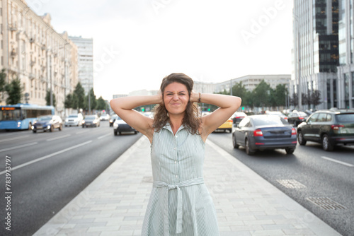 Urban environment. Car and city noise. A girl stands against the backdrop of the city, frowns and covers her ears with her hands.