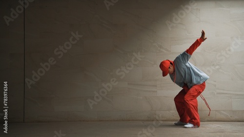 Handsome choreographer practice street dance in gray background. Young attractive b boy dancer perform while wearing stylish cloth. Feeling of lively step. Copy space. Outdoor sport 2024. Sprightly.