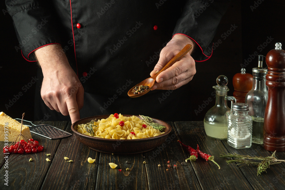 The chef adds aromatic spices or dry pepper with a spoon to a bowl of pasta on the kitchen table. Low key concept of preparing a delicious breakfast in the cook room