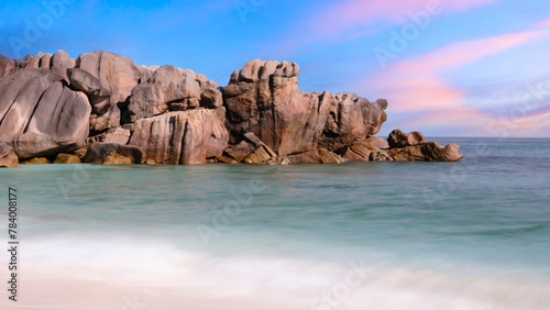 A rocky shoreline with a calm ocean in the background. The sky is a mix of blue and pink, creating a serene and peaceful atmosphere