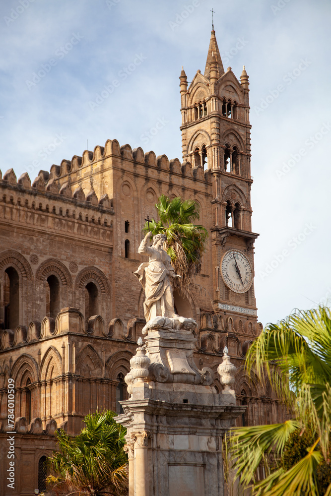 Statue of Santa Rosalia stands before the ornate Palermo Cathedral, nestled among lush greenery under the Sicilian sky, Sicily, Italy