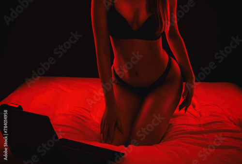 A young webcam model girl is sitting in front of a laptop. She communicates on a white bed in the bedroom.