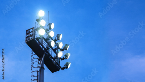 A floodlight tower illuminated, standing tall against the evening blue sky background with copy space. © Topuria Design