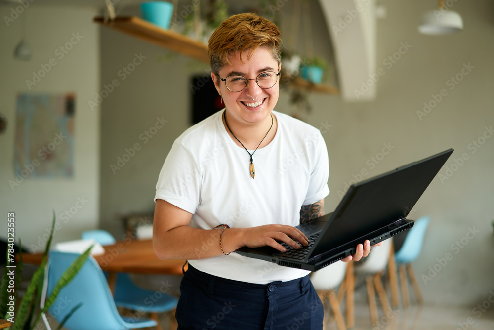 custom made wallpaper toronto digitalSmiling transgender professional holds laptop, works happily in modern office space. Inclusive workplace, young trans person enjoys career, experiences job fulfillment with tech in eco-friendly area.