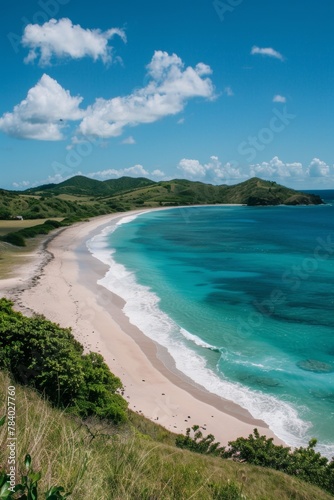 A panoramic view of a long, pristine beach stretching towards the horizon, flanked by lush green hills and crystal-clear turquoise water