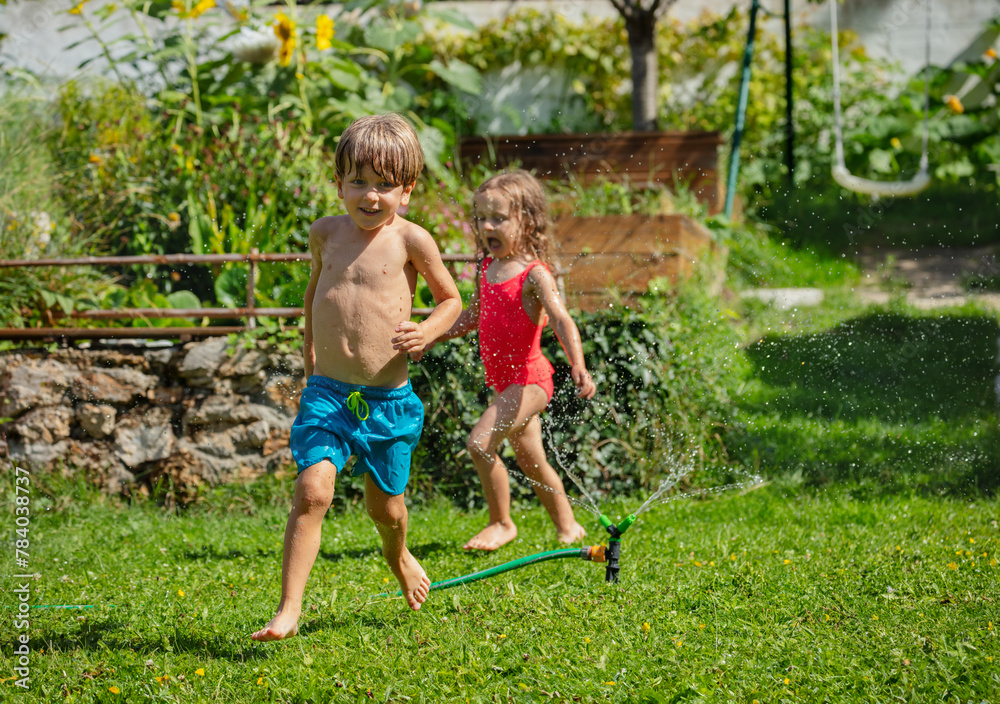 Fototapeta premium Playful boy and girl enjoying a sprinkle of water run around