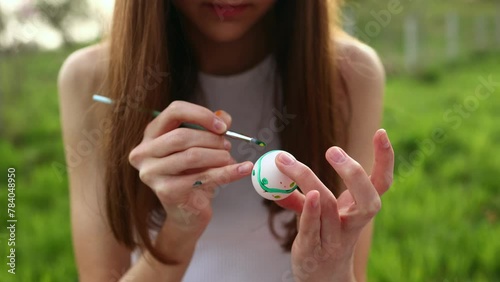 Girls' hands paint Easter eggs with paints of different colors in the open air. Watercolor painting on eggs. Close-up video of hands