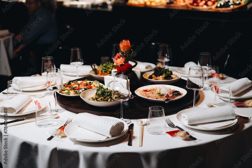 Fototapeta premium Beautifully organized event - round served table banquet ready for guests, round decorated table with empty plate, glasses, forks, napkin. Elegant dinner table 