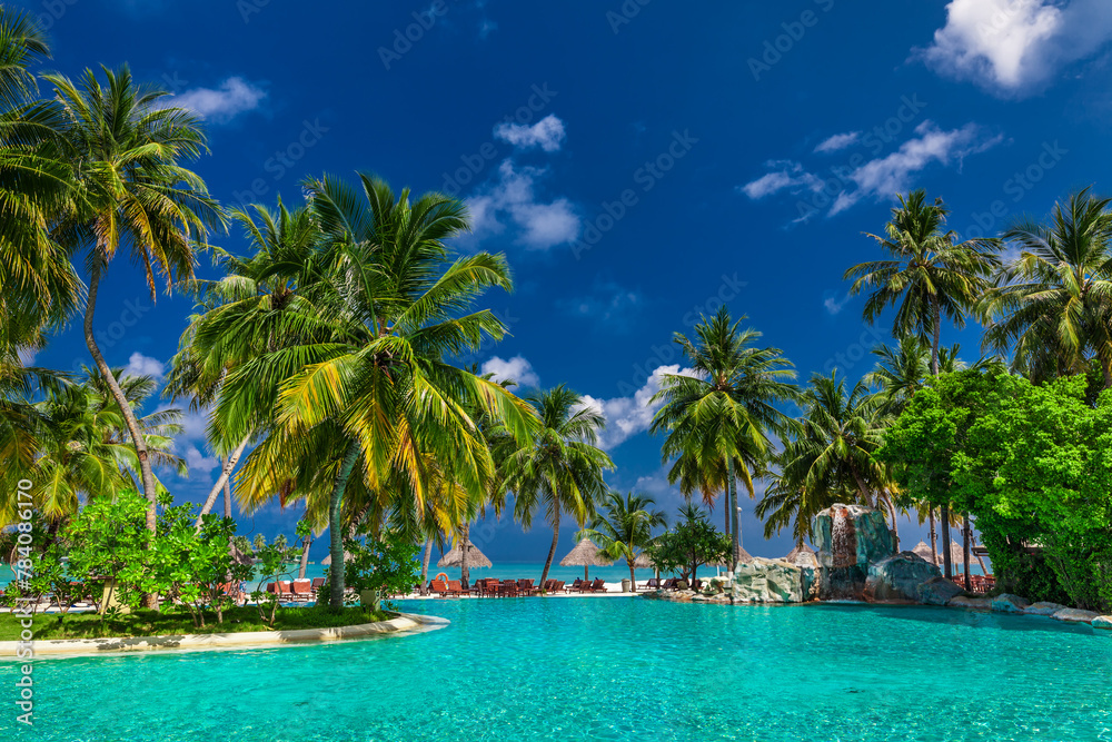 Large infinity swimming pool on the beach with palm trees and umbrellas