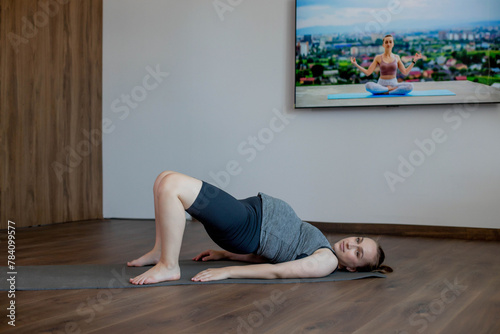 Pregnant woman exercing yoga at home. Lies on his back and lifts up. photo