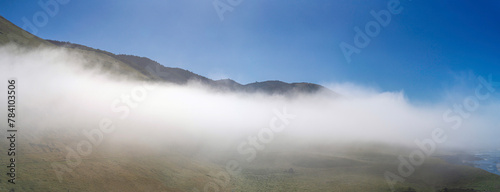 panorama of mountains, pasture, ocean in fog, clouds