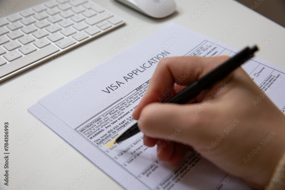 Close up of a black pan on visa application document, on table with computer keyboard and a mouse Close up of a black pan on visa application document, on table with computer keyboard and a mouse
