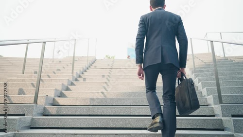 Shot from behind of young business man walking up the stairs  to work, salary man daily routine, low angle shot working man holding business bag, urban commuter, salary man walking to work, low angle