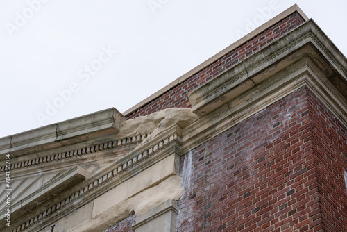 Example of crumbling, deteriorating ornamental precast concrete elements, features, on an old brick school building.