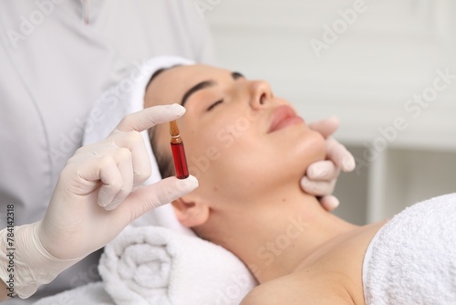 Professional cosmetologist holding skincare ampoule while working with client in clinic, closeup