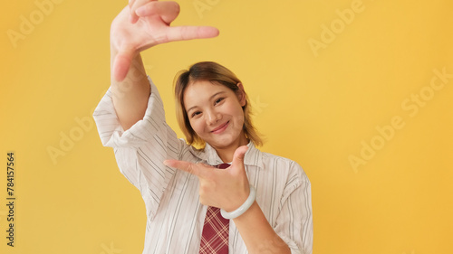 Young woman looking at camera shows compositional gesture, isolated on yellow background photo