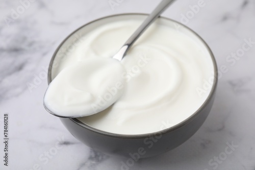 Delicious natural yogurt in bowl and spoon on white marble table, closeup