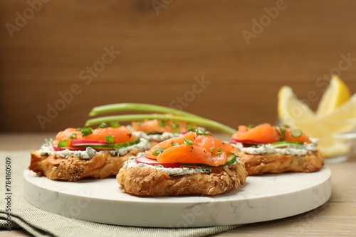 Tasty canapes with salmon, cucumber, radish and cream cheese on wooden table