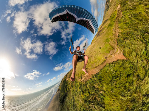 Extreme paragliding pilot soaring in the New Zealand beach at sunset. Adventure concept