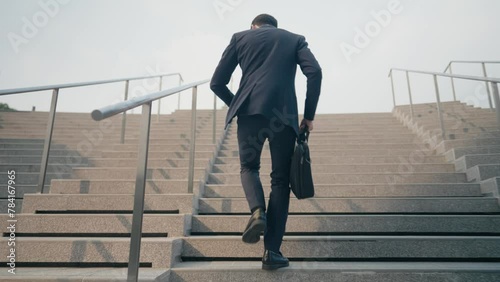 Follow shot of young businessman running up the stairsway rushing to work, salary man routine, working man holding business bag off to work, urban commuter being late to office, work punctuality  photo