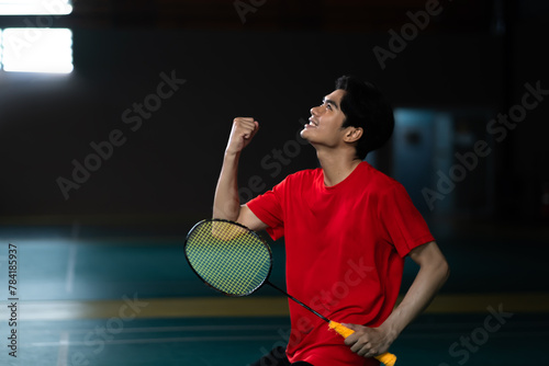 Badminton player side view celebrating victory, holding a racket, and cheering with overwhelming excitement. Male athlete wearing a red shirt, Sport activity and challenging concepts.