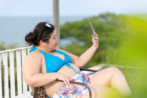 Asian Plus Soze Woman Wearing Bikini Using Mobile Phone to Selfie Herself While Vacation at Sea in Summer. Concept of Positive Body Figure.