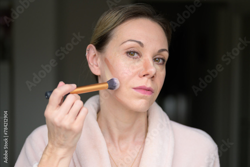 Blonde woman applying makeup with a brush