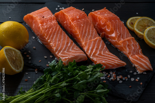 Fresh raw salmon fillet with cooking ingredients, herbs and lemon on black slate