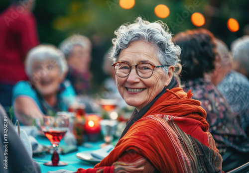 A smiling senior woman sitting at a table with friends during a backyard party © Kien