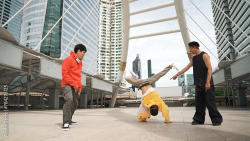 Group of professional happy street dancer cheer up while asian hipster perform b boy dance at urban city surrounded by people with low angle camera. Break dance concept. Outdoor sport 2024. Sprightly.