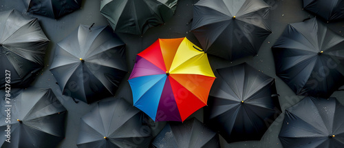 Artistic portrayal of a lone rainbow umbrella among numerous black ones photo