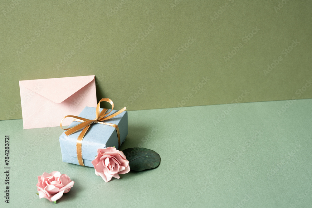Blue gift box and envelope card with pink rose on green table. khaki wall background. birthday celebration concept