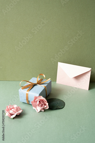 Obraz na płótnie Blue gift box and envelope card with pink rose on green table. khaki wall background. birthday celebration concept w salonie