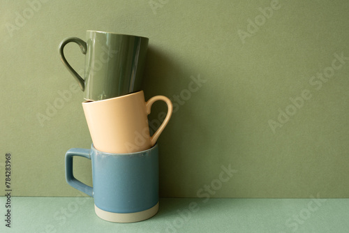 Stack of ceramic mug cups on green table. khaki wall background