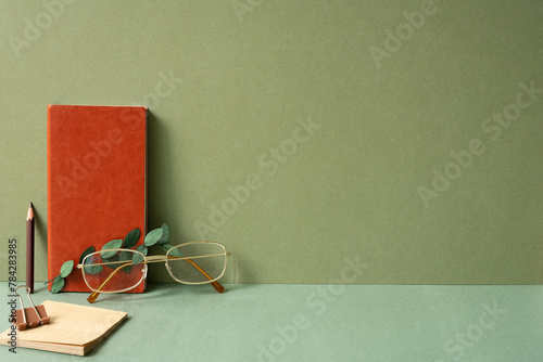 Workspace diary note, notepad, clip, pencil, eyeglasses, eucalyptus leaf on green desk. khaki wall background