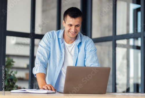 Successful Business man Entrepreneur in a shirt standing near workplace working using laptop in an modern office