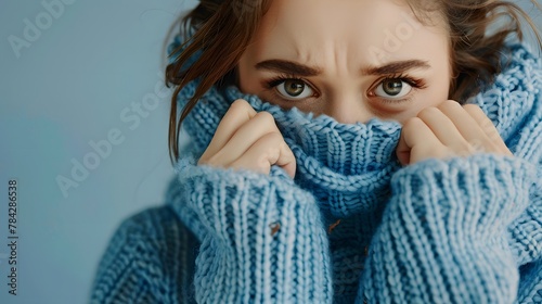 A woman wearing a blue turtleneck knitted sweater with eyes downcast as she covers her sad face with her hands