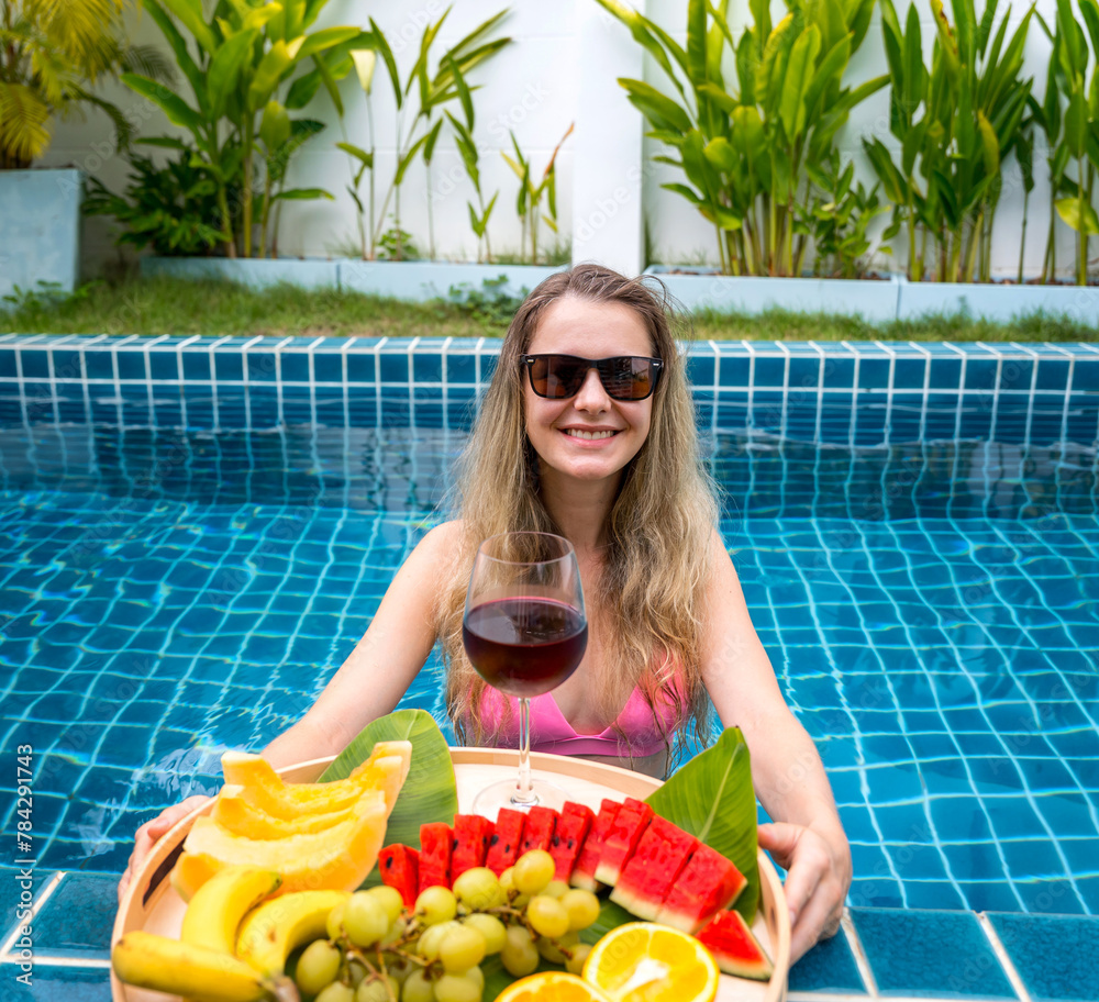 Beautiful woman in the swimming pool with glass of wine and floating tray of fruits Beautiful woman in the swimming pool with glass of wine and floating tray of fruits