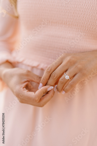 Round engagement ring on woman's hand in pink dress