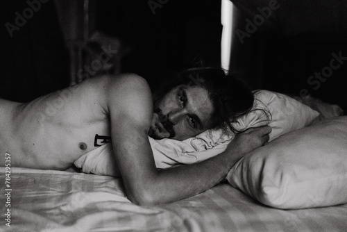 Naked young man is looking at camera while lying in bed. photo